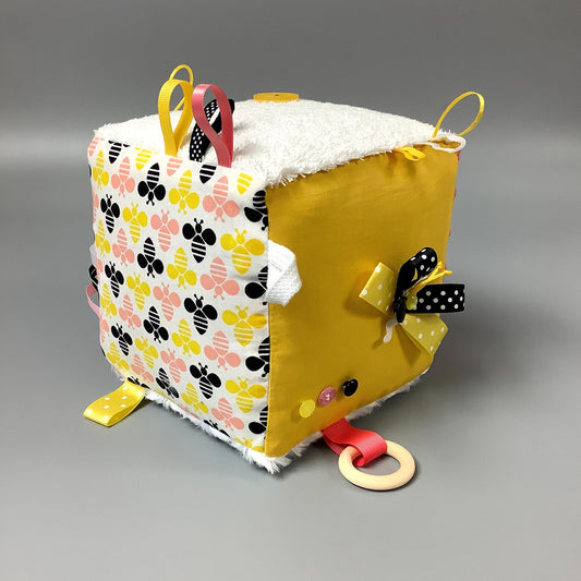 Cube d'éveil pour enfant  Fait en coton avec rubans et petits accessoires de bois. Le cube fait du bruit lorsqu'il est agité.  Ce produit unique est fait au Québec.