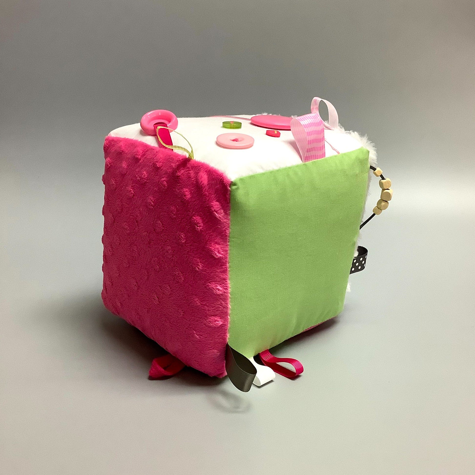 Cube d'éveil pour enfant  Fait en coton avec rubans et petits accessoires de bois. Le cube fait du bruit lorsqu'il est agité.  Ce produit unique est fait au Québec.