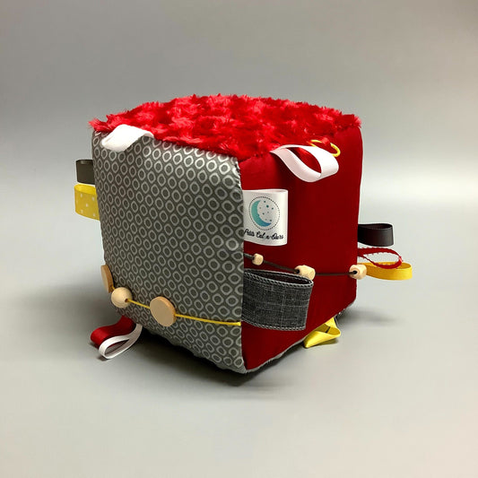 Cube d'éveil pour enfant  Fait en coton avec rubans et petits accessoires de bois. Le cube fait du bruit lorsqu'il est agité.  Ce produit unique est fait au Québec.