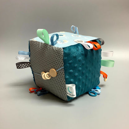 Cube d'éveil pour enfant  Fait en coton avec rubans et petits accessoires de bois. Le cube fait du bruit lorsqu'il est agité.  Ce produit unique est fait au Québec.