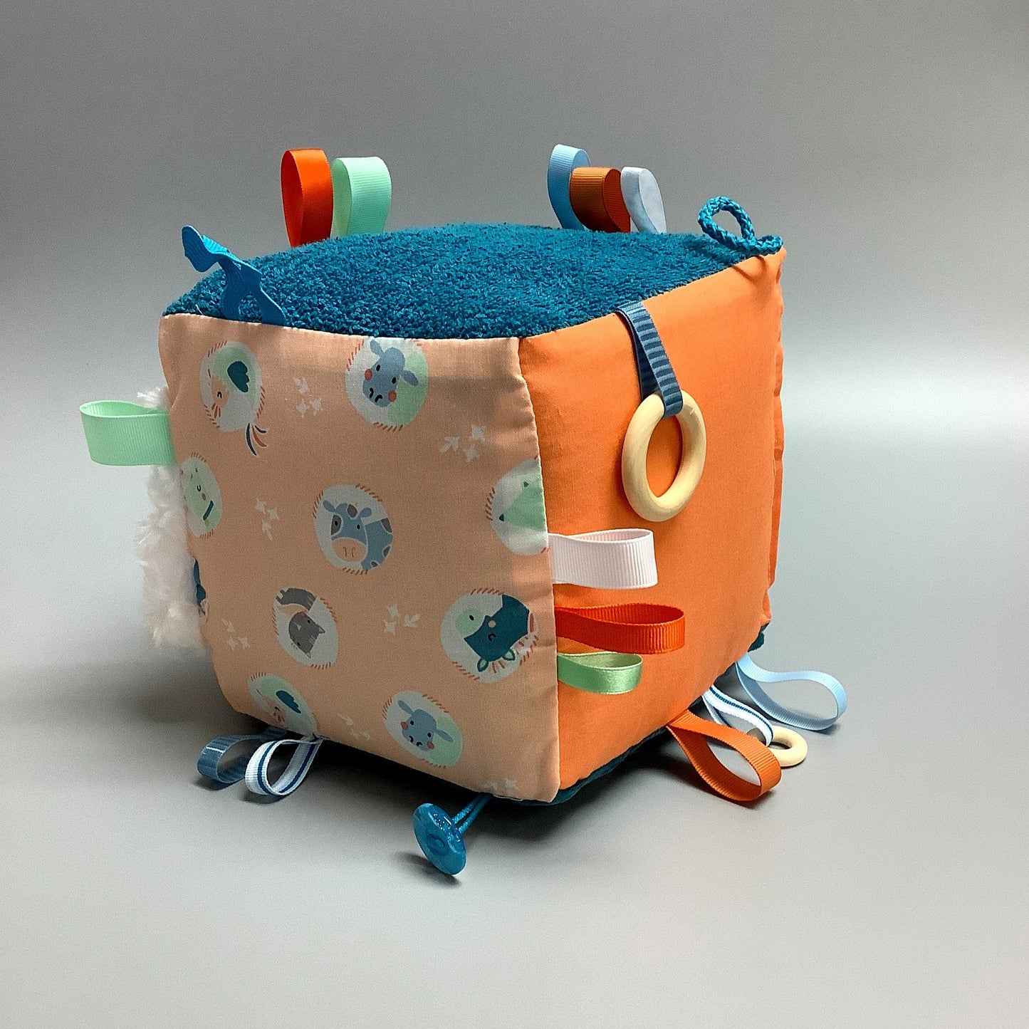 Cube d'éveil pour enfant  Fait en coton avec rubans et petits accessoires de bois. Le cube fait du bruit lorsqu'il est agité.  Ce produit unique est fait au Québec.