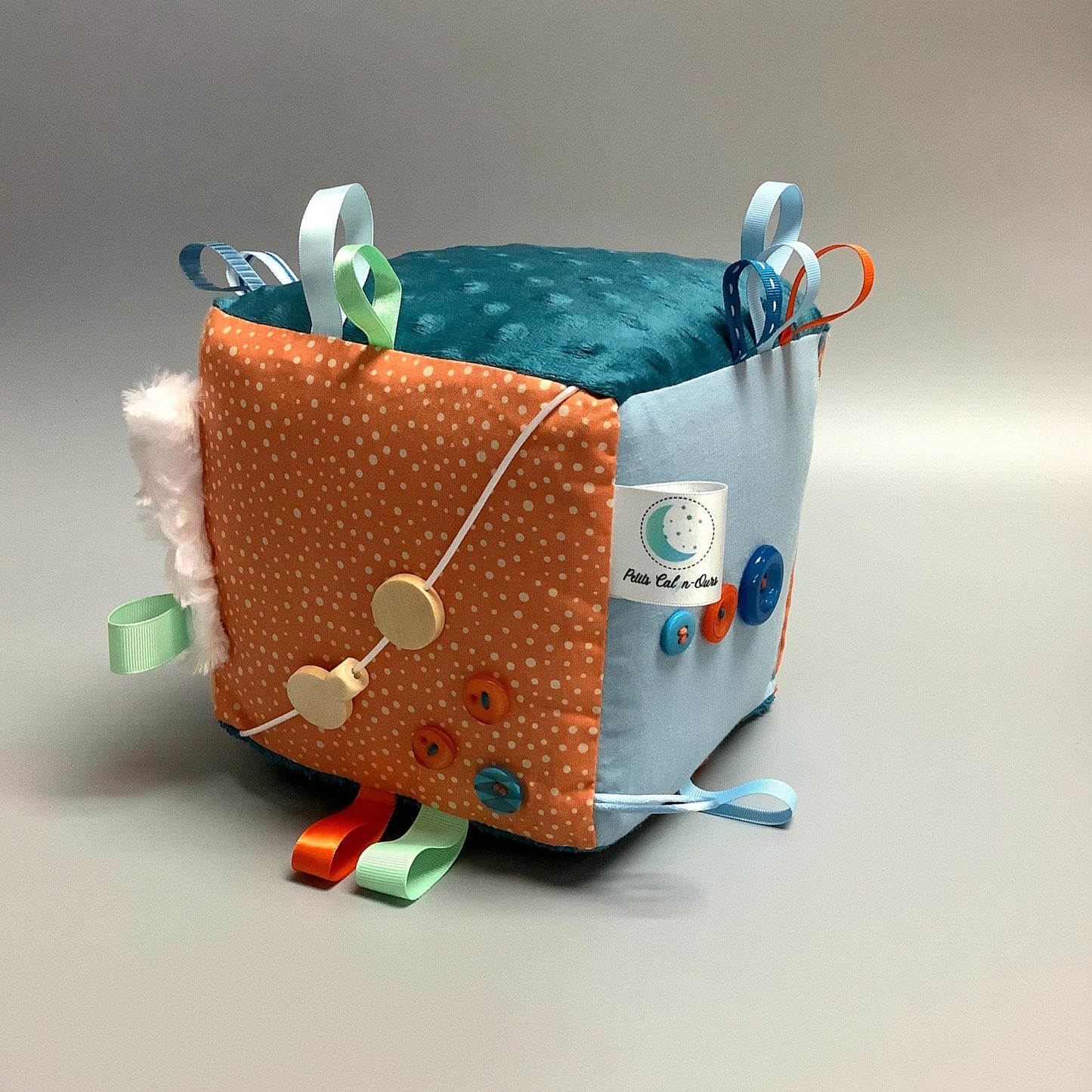 Cube d'éveil pour enfant  Fait en coton avec rubans et petits accessoires de bois. Le cube fait du bruit lorsqu'il est agité.  Ce produit unique est fait au Québec.