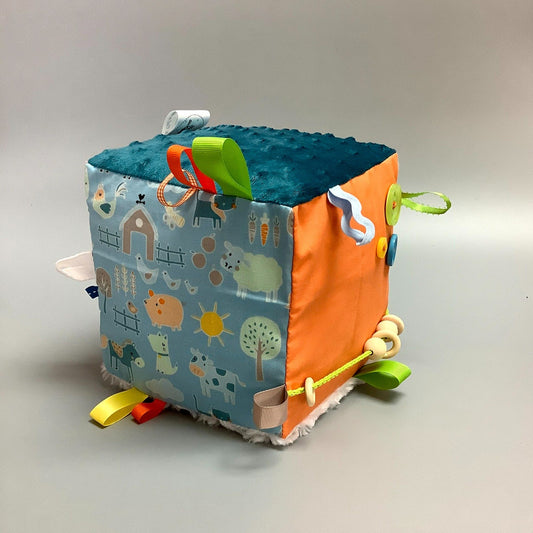 Cube d'éveil pour enfant  Fait en coton avec rubans et petits accessoires de bois. Le cube fait du bruit lorsqu'il est agité.  Ce produit unique est fait au Québec.