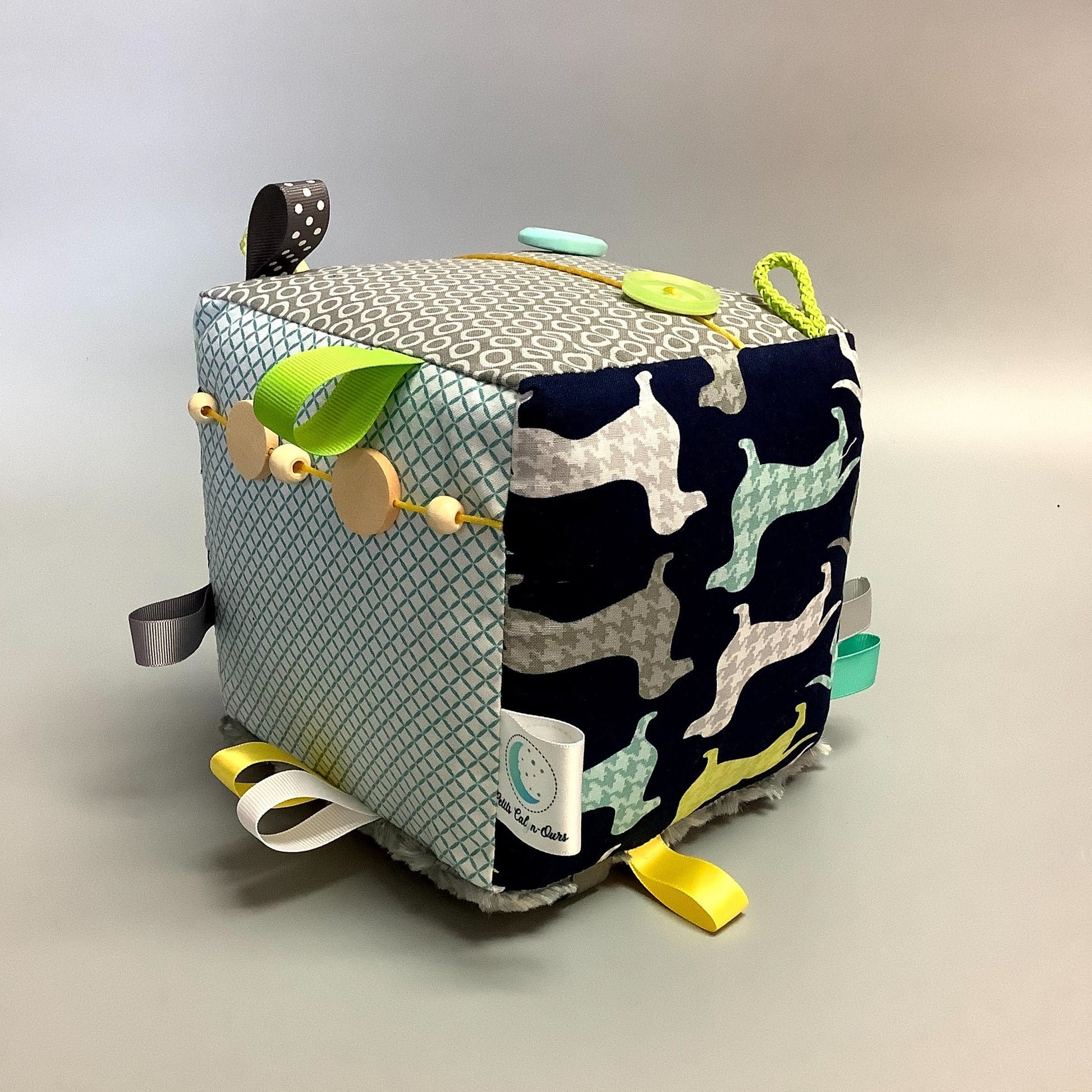 Cube d'éveil pour enfant  Fait en coton avec rubans et petits accessoires de bois. Le cube fait du bruit lorsqu'il est agité.  Ce produit unique est fait au Québec.