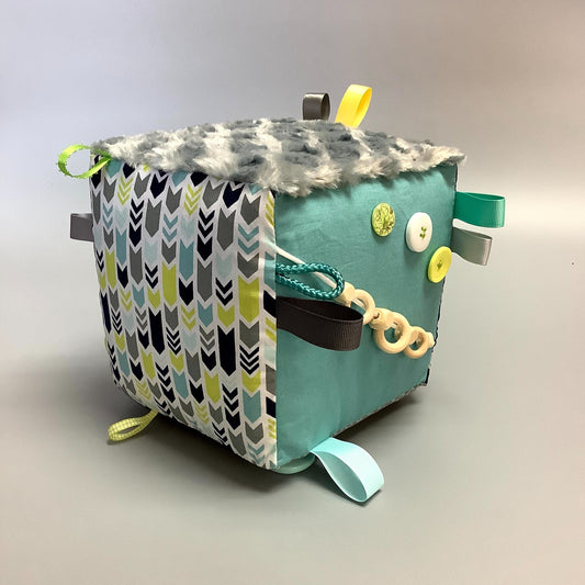 Cube d'éveil pour enfant  Fait en coton avec rubans et petits accessoires de bois. Le cube fait du bruit lorsqu'il est agité.  Ce produit unique est fait au Québec.