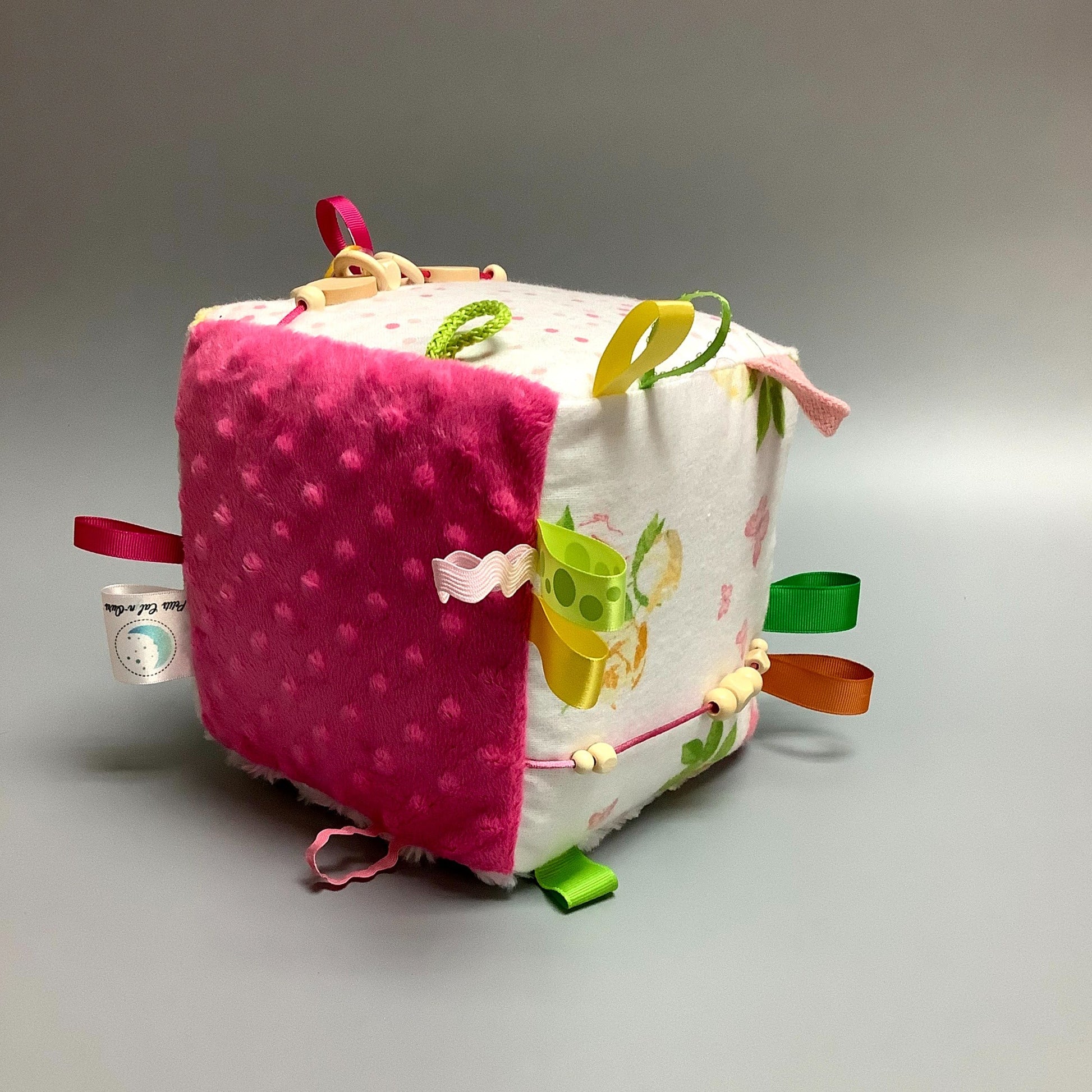 Cube d'éveil pour enfant  Fait en coton avec rubans et petits accessoires de bois. Le cube fait du bruit lorsqu'il est agité.  Ce produit unique est fait au Québec.