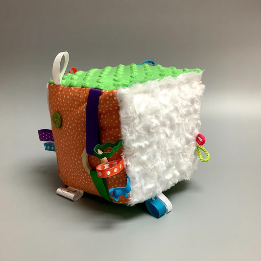 Cube d'éveil pour enfant  Fait en coton avec rubans et petits accessoires de bois. Le cube fait du bruit lorsqu'il est agité.  Ce produit unique est fait au Québec.
