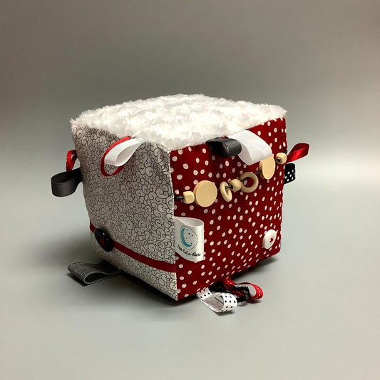 Cube d'éveil pour enfant  Fait en coton avec rubans et petits accessoires de bois. Le cube fait du bruit lorsqu'il est agité.  Ce produit unique est fait au Québec.
