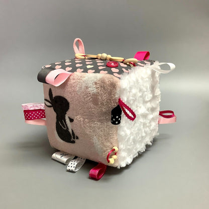Cube d'éveil pour enfant  Fait en coton avec rubans et petits accessoires de bois. Le cube fait du bruit lorsqu'il est agité.  Ce produit unique est fait au Québec.