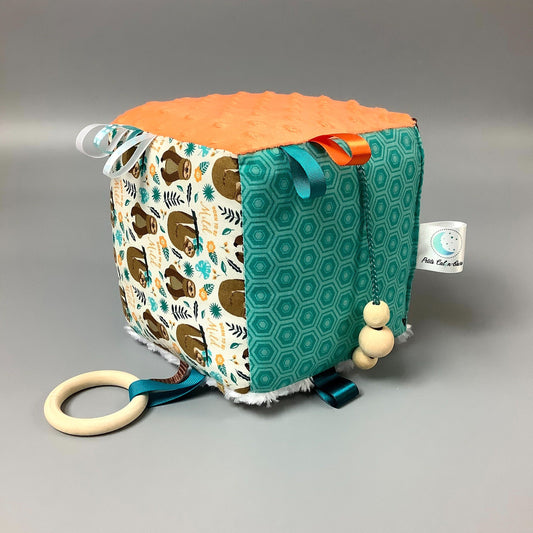 Cube d'éveil pour enfant  Fait en coton avec rubans et petits accessoires de bois. Le cube fait du bruit lorsqu'il est agité.  Ce produit unique est fait au Québec.