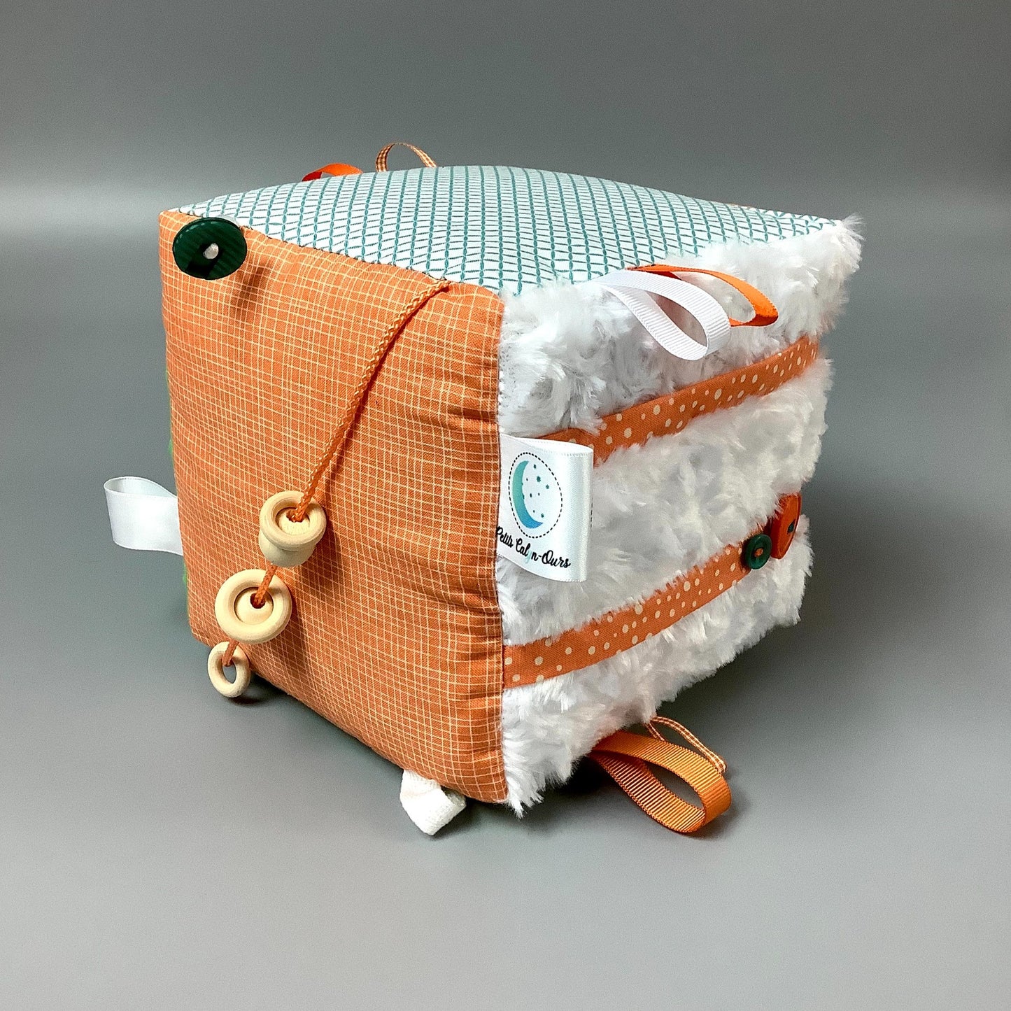 Cube d'éveil pour enfant  Fait en coton avec rubans et petits accessoires de bois. Le cube fait du bruit lorsqu'il est agité.  Ce produit unique est fait au Québec.