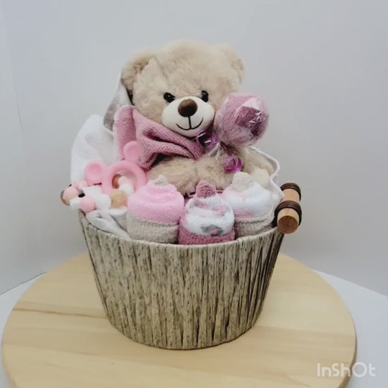 Vidéo 360 de l'Ensemble cadeau pour babyshower de bébé fille. Un panier contenant un toutou ourson beige, une couverture en flanelle des débarbouillettes disposées en cupecake et des bas en forme de suçon. Complété d'un jouet de dentition en silicone.